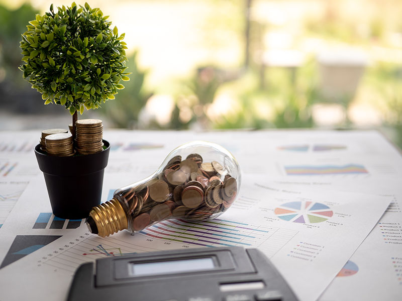 Energie sparen: Münzen in Glühbirne auf Unterlagen