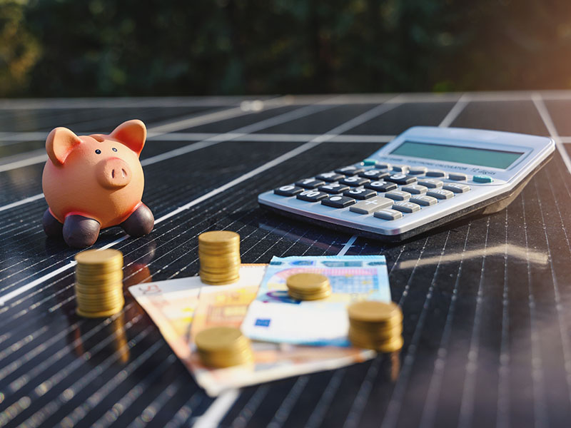 Sparschwein, Geld und Taschenrechner liegen auf Solarpanel